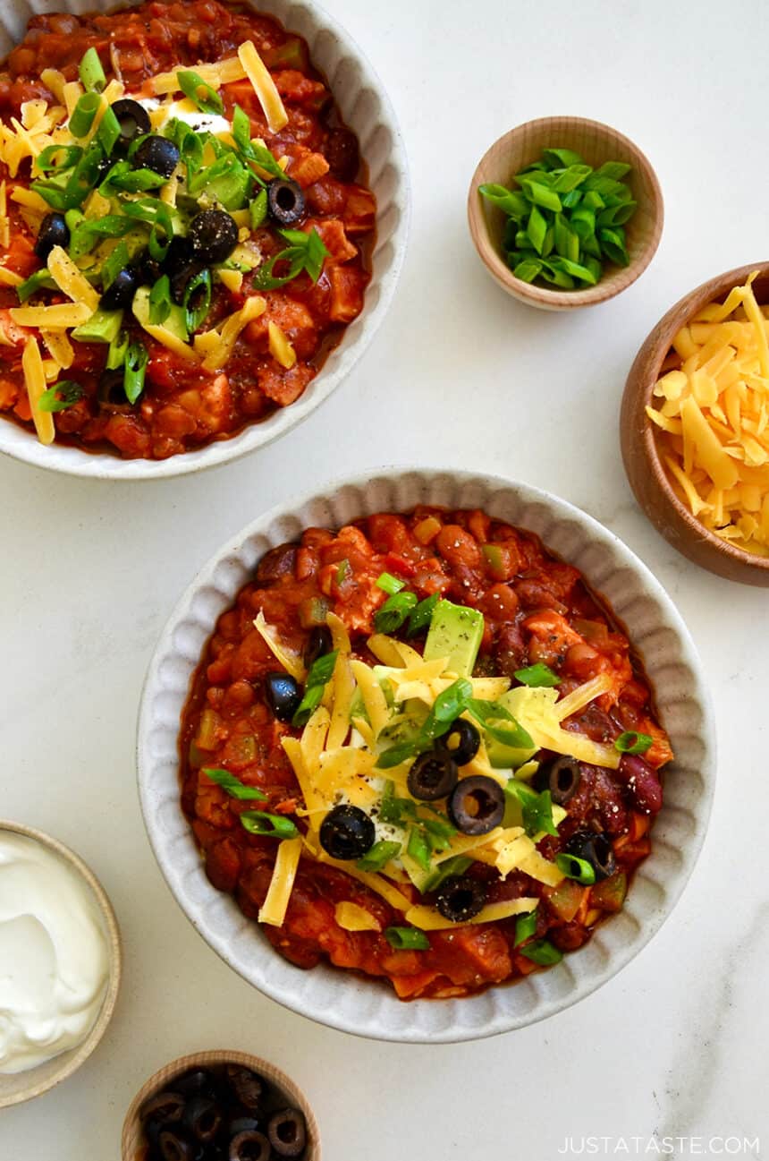 Leftover turkey chili servings in bowls topped with cheddar cheese, olives, chives and avocado slices. 