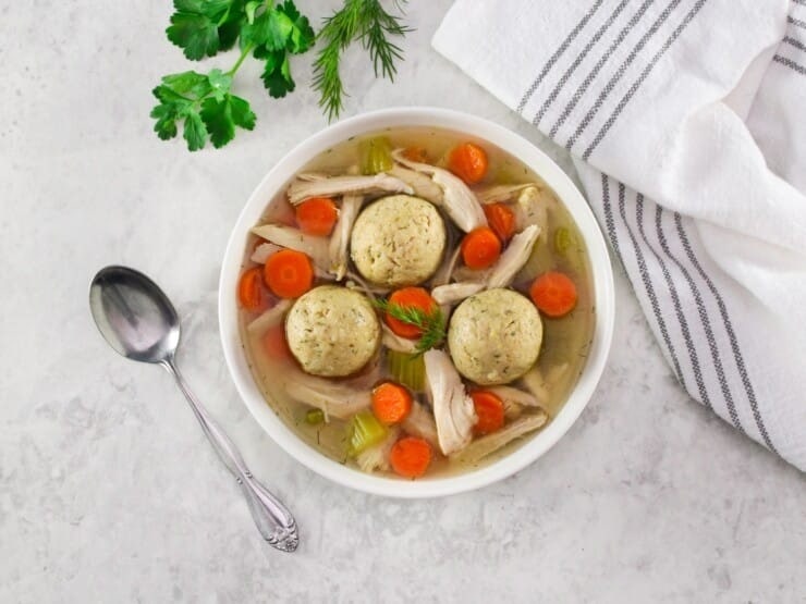 Bowl of Matzo ball chicken soup on a bowl made with carrots, dough balls and shredded chicken.