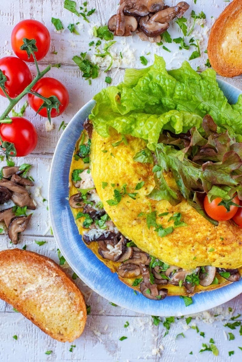 Egg omlette with mushroom filling served on a blue plate with veggies. 