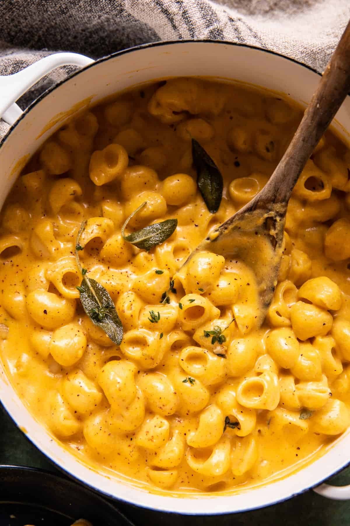 Pumpkin mac and cheese on a pot mixed with a wooden ladle spoon. 