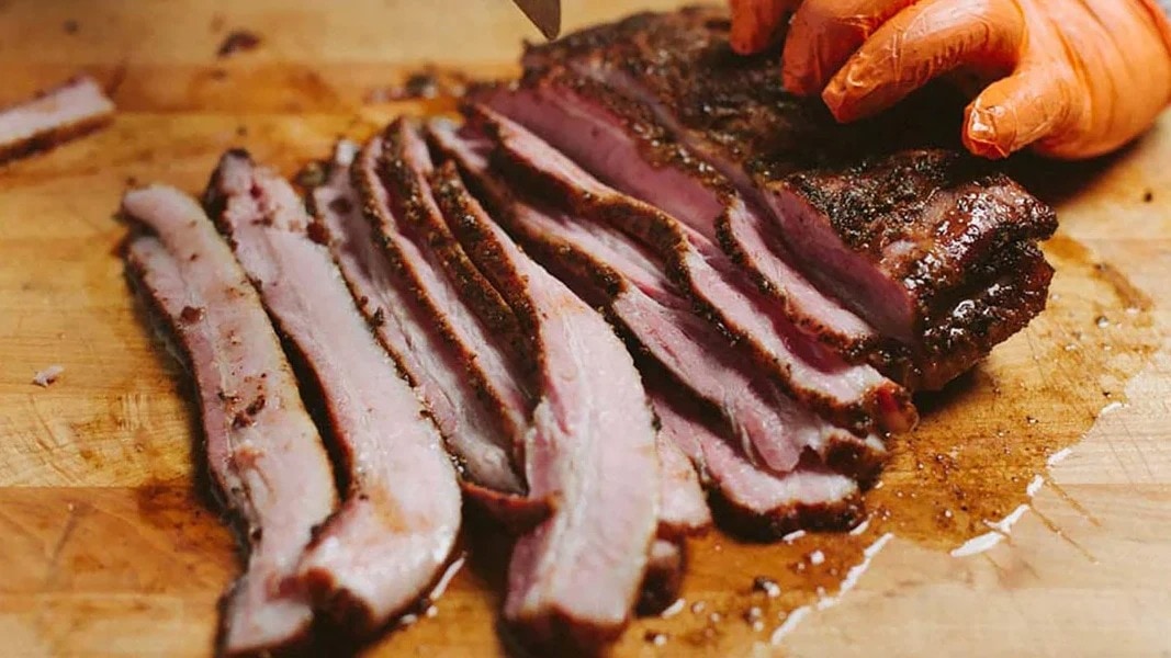 Slices of Pork Belly Pastrami on a wooden cutting board