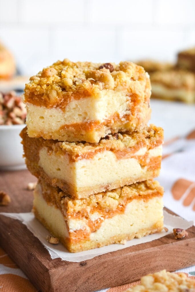 Stack of pumpkin cheesecake bars on top of wooden cutting board. 