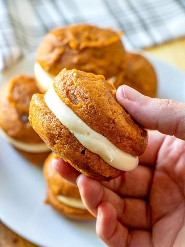 Hand holding pumpkin whoopie pies with cream cheese frosting. 