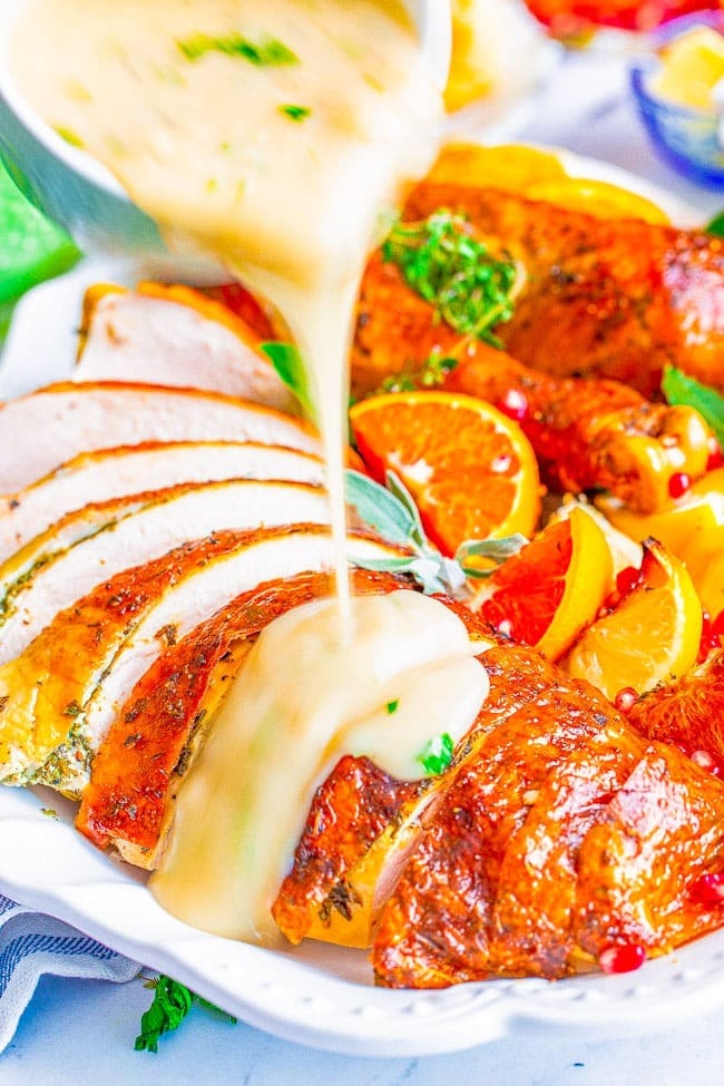 Gravy pouring to a sliced baked turkey on a plate garnished with sliced lemon. 