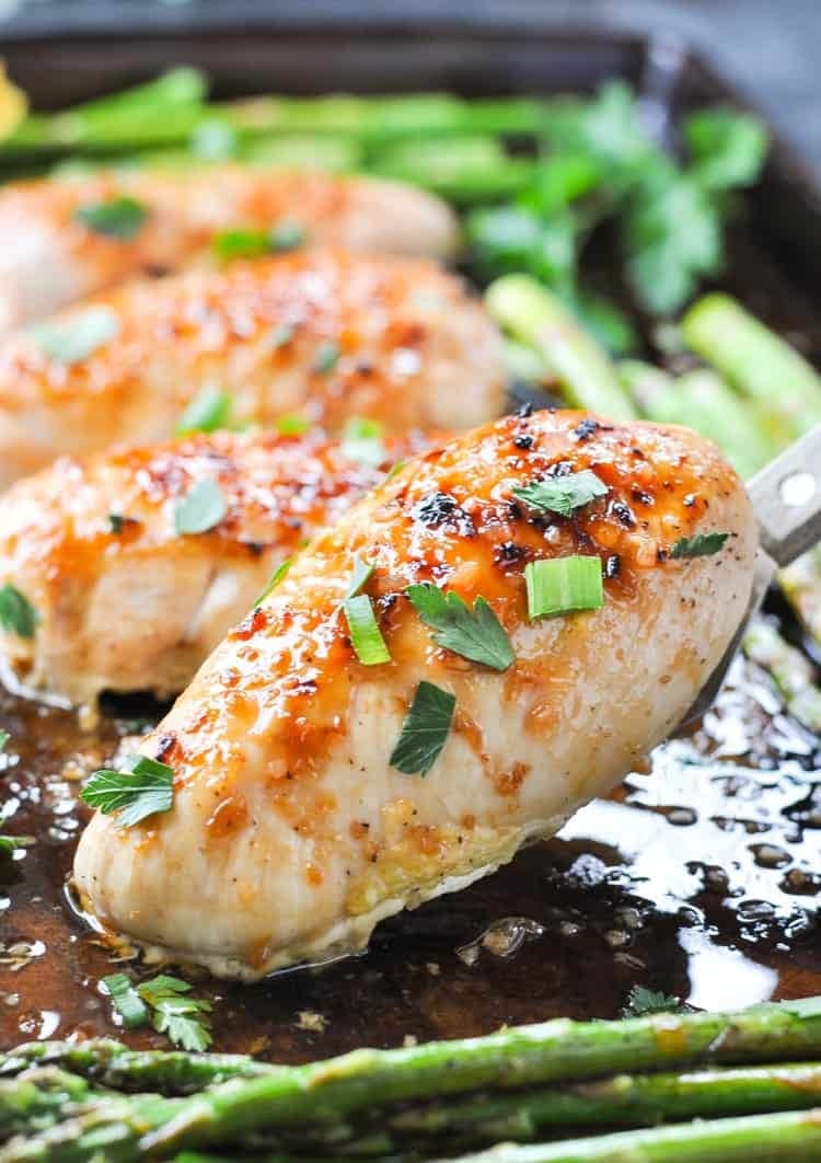 Chicken breast and asparagus cooked in a sheet pan with with orange juice, honey, garlic, and soy sauce garnished with chopped parsley. 