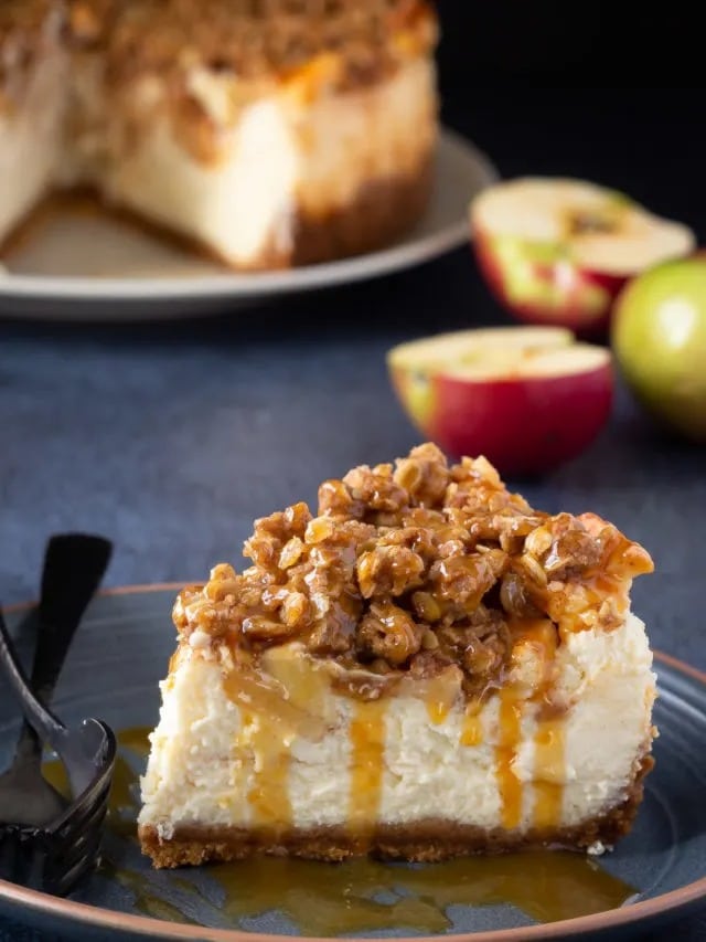Slice of apple crisp cheesecake topped with caramel and crumbles. 