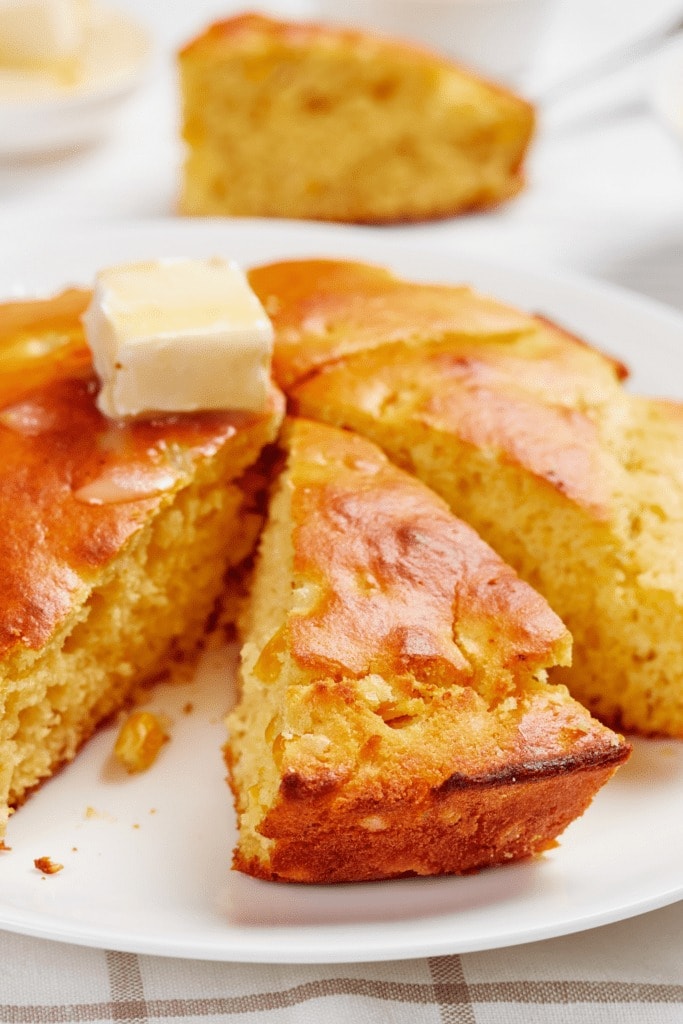 Sliced Albers cornbread served on a white plate topped with a slice of a butter. 