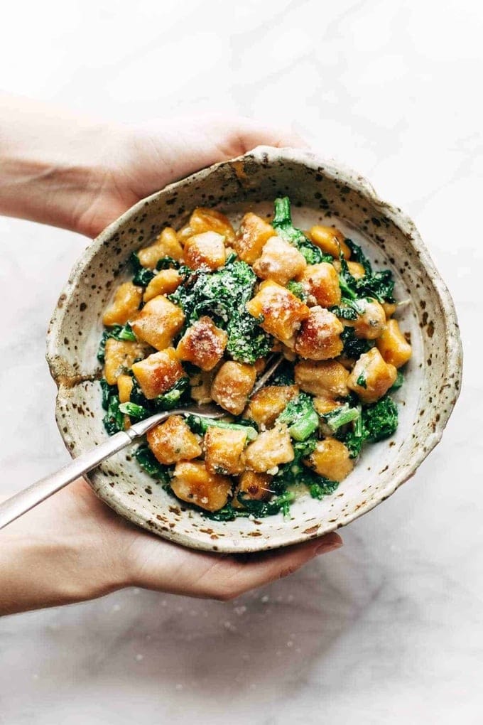 Hand holding a bowl of sweet potato gnocchi with broccoli rabe and garlic sage butter sauce.