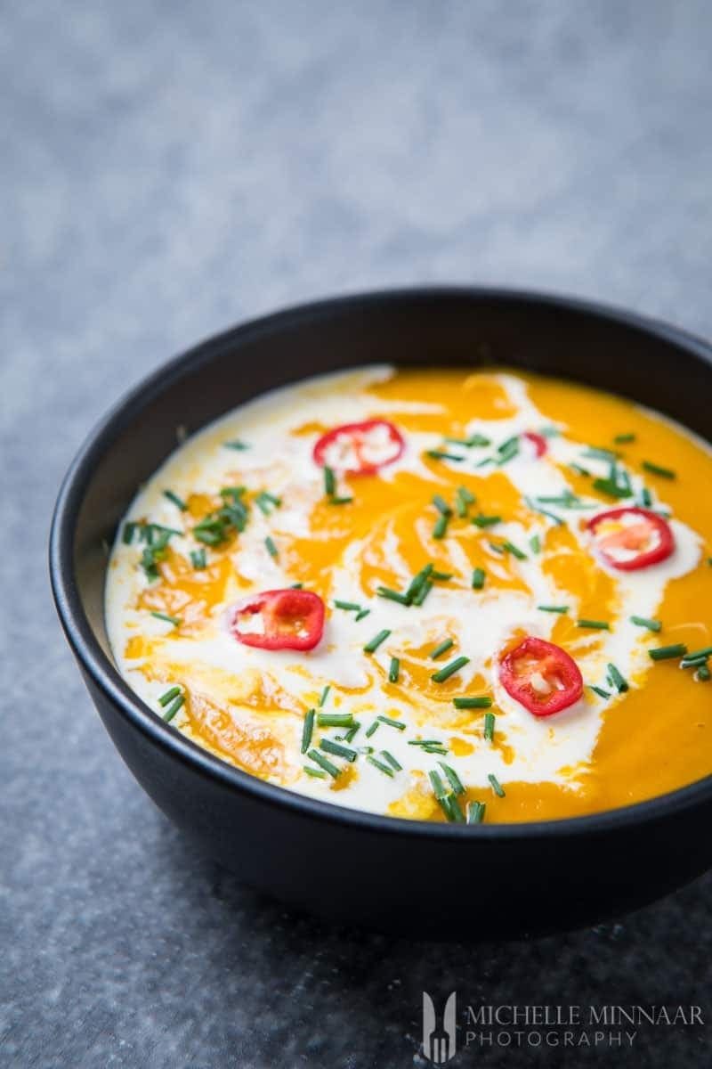 Sweet potato soup in a black bowl garnished with chives and chiles. 