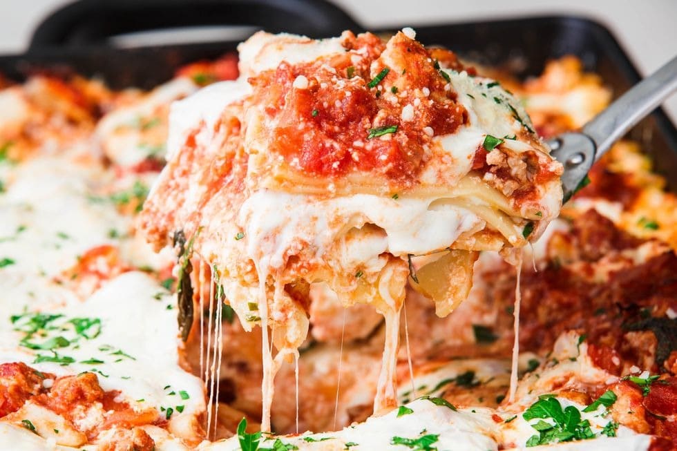 A cheesy lasagna casserole being lifted from the dish, revealing its layers