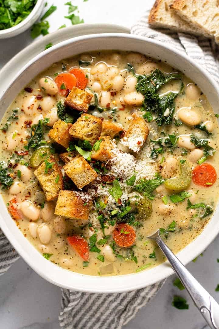 Bowl of homemade White Bean Soup with chopped carrots, celery, white beans, kale, dried oregano, thyme and sage