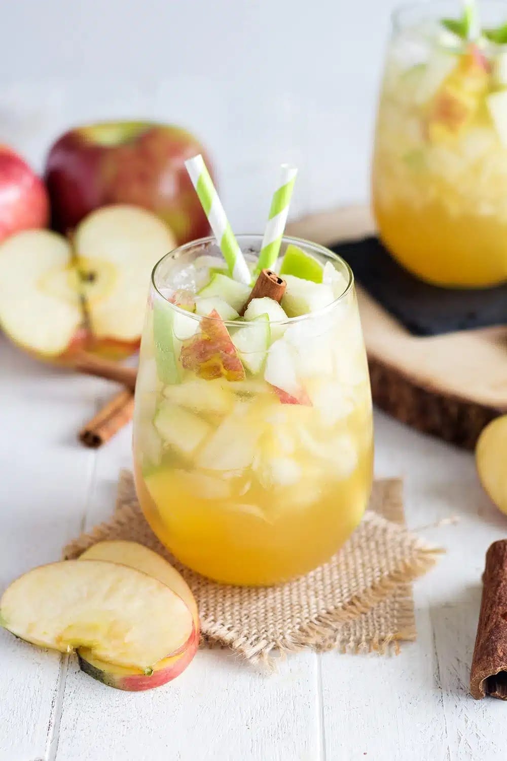 Glass of iced apple pie sangria with sliced apple and cinnamon sticks. 