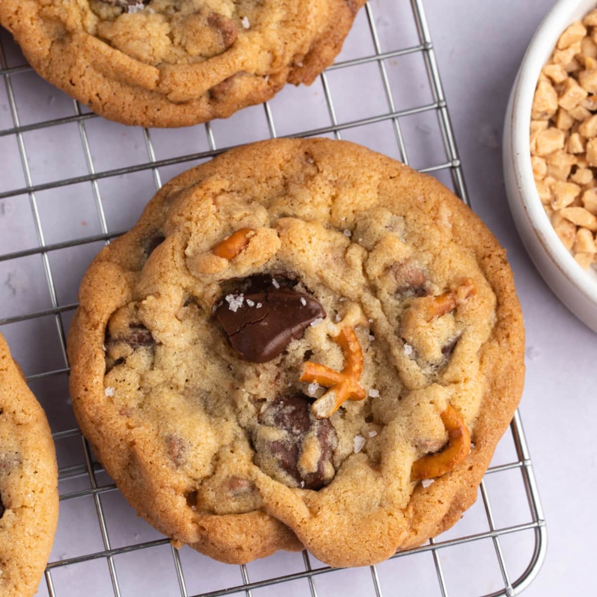 Closeup of kitchen sink cookies topped with pretzels and salt on a cooling rack.