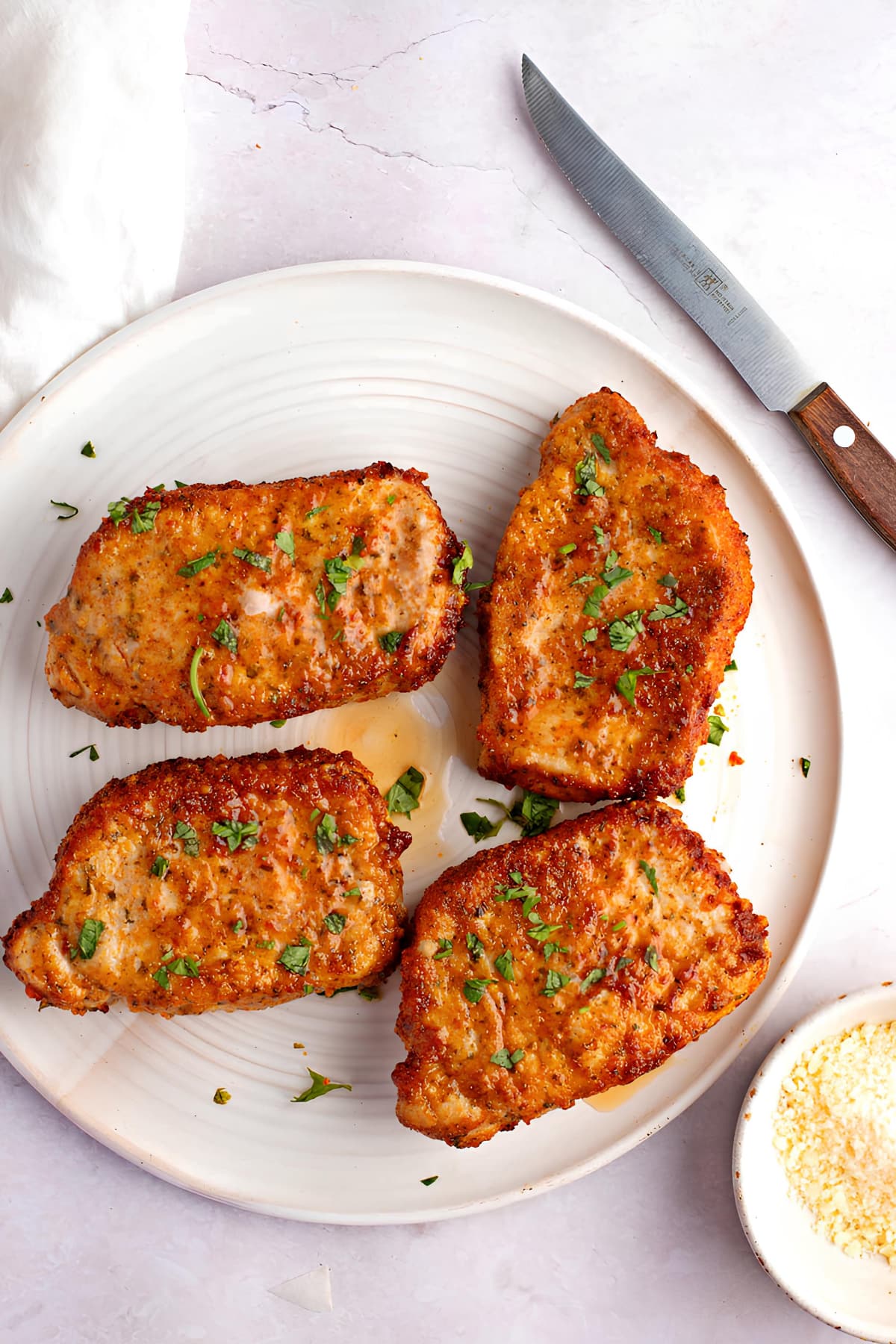 Air Fryer Pork Chops Recipe: Four servings of breaded and seasoned pork chops served on white plate. 