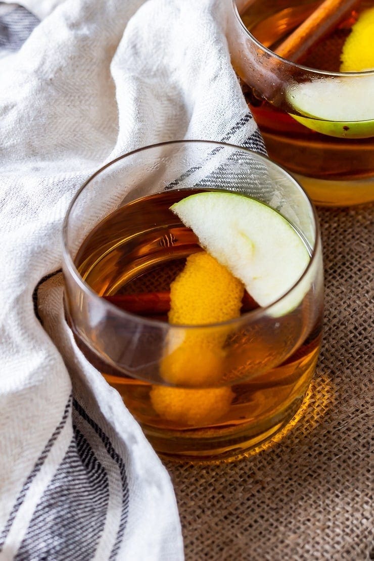 Apple juice on a glass mug with slices of green apple, orange peel and cinnamon stick.