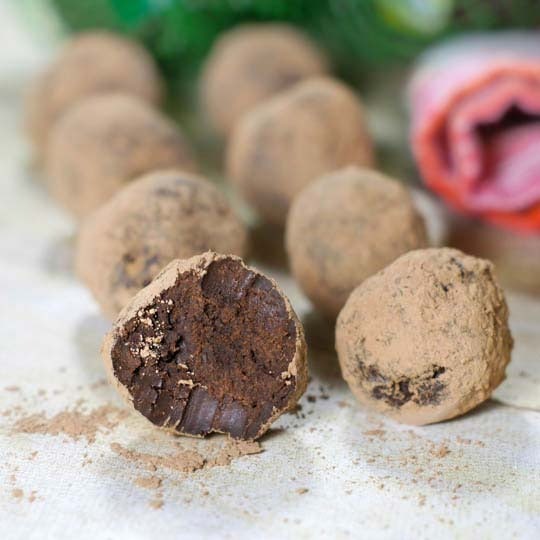 Whole and one piece bitten chocolate truffles laid on white surface. 