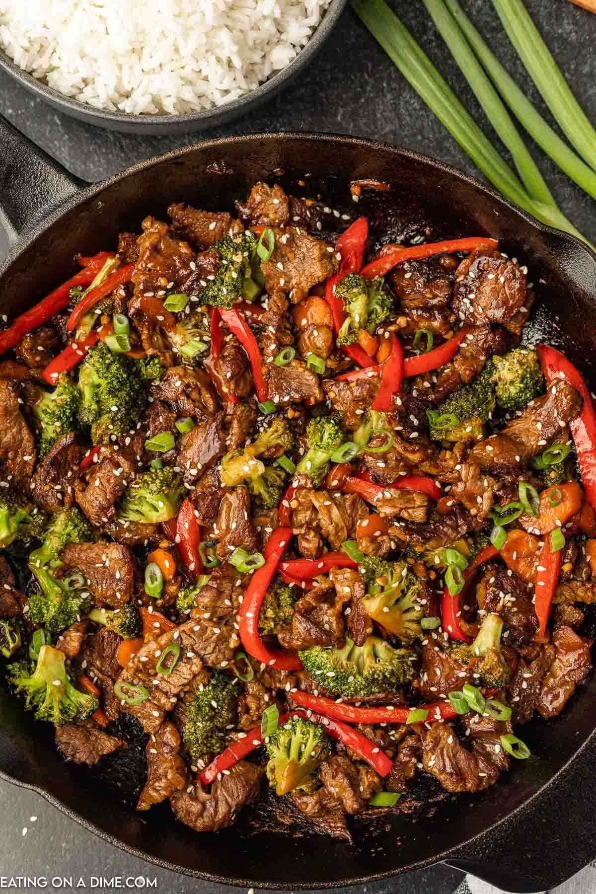 Stir fried tender beef stripes with carrots, bell pepper, cauliflower, garnished with chopped green onions and sesame seeds on a cast iron pan