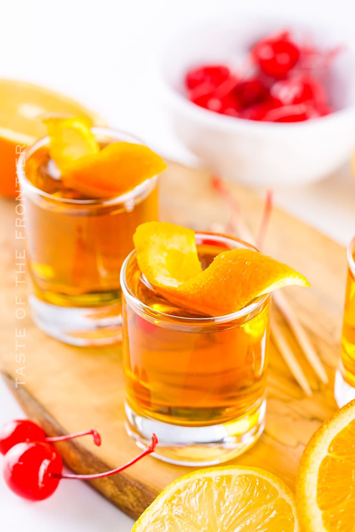 Three homemade three wise men shots with jack daniels and johnny walker, garnished with an orange peel, served in a flight on a wooden tray