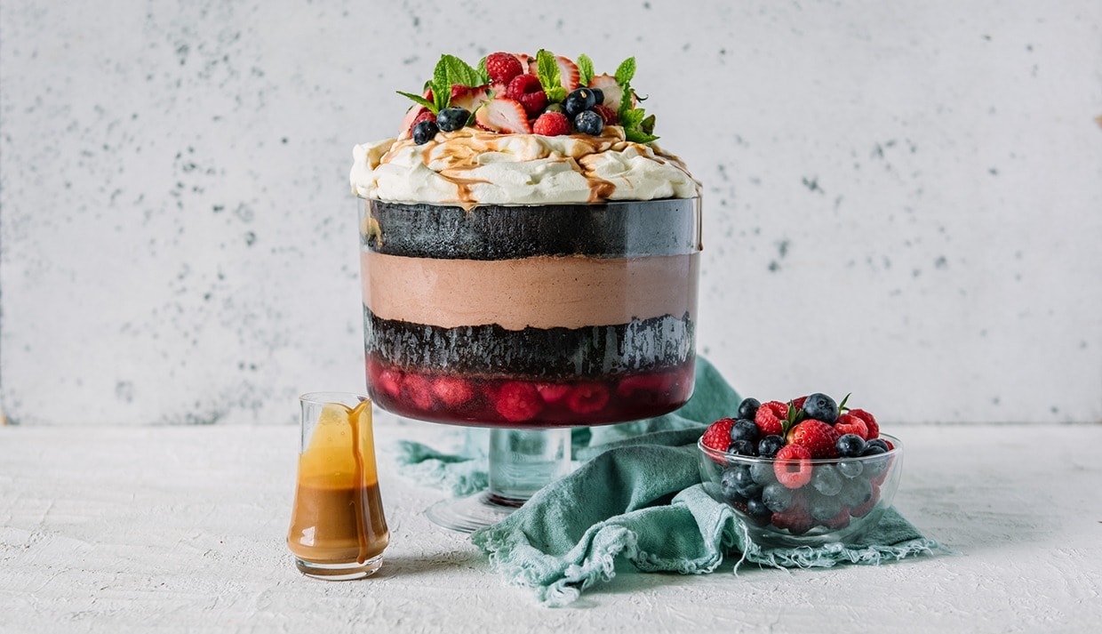 Chocolate Guinness cake  layered with chocolate cream and strawberry pudding on a trifle bowl topped with whipped cream and fresh berries.