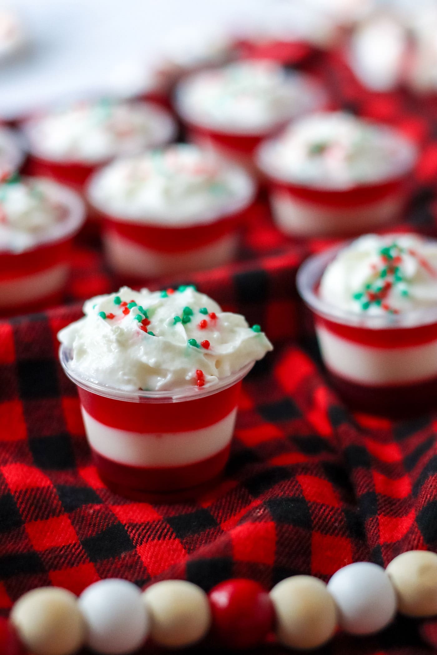Candy cane strips Jello shots on plastic cups with whipped cream and sprinkles on top. 