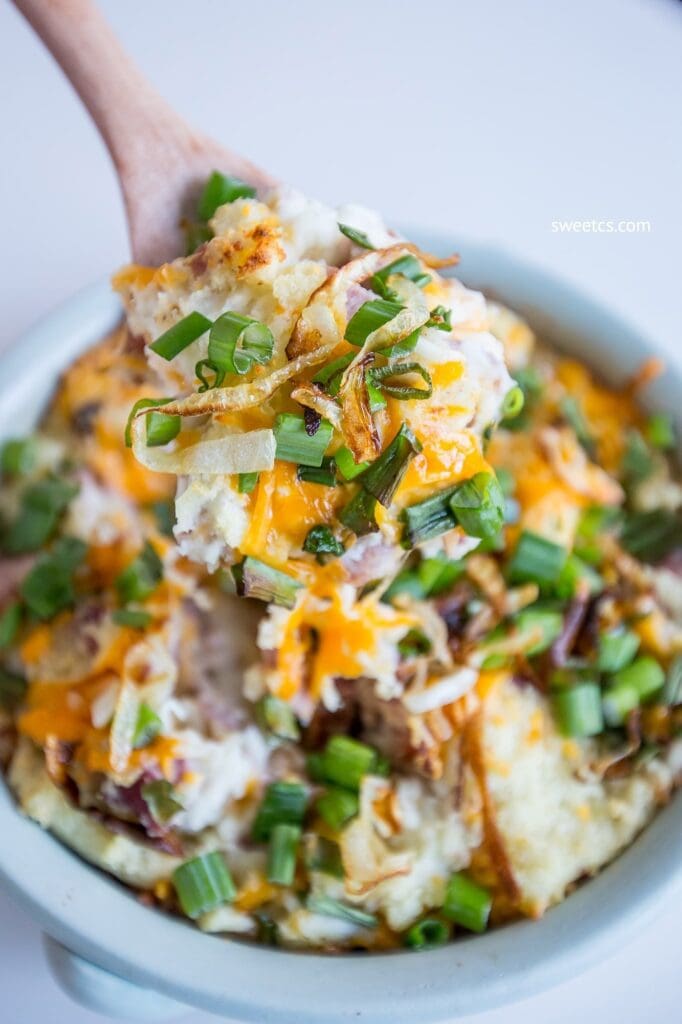 Wooden spoon full of a scoop of mashed potato and ham casserole with lots of onion chives. 