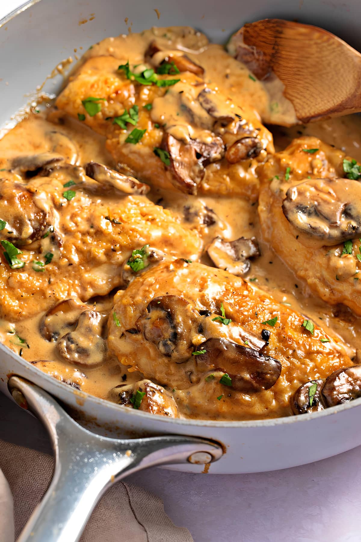 Chicken breast with marsala sauce garnished with chopped parsley cooked in a stainless steel pan.