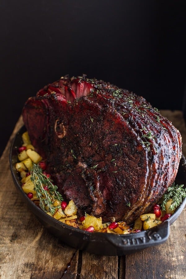 Seasoned whole glazed ham with a bed of pineapple chunks on a skillet.