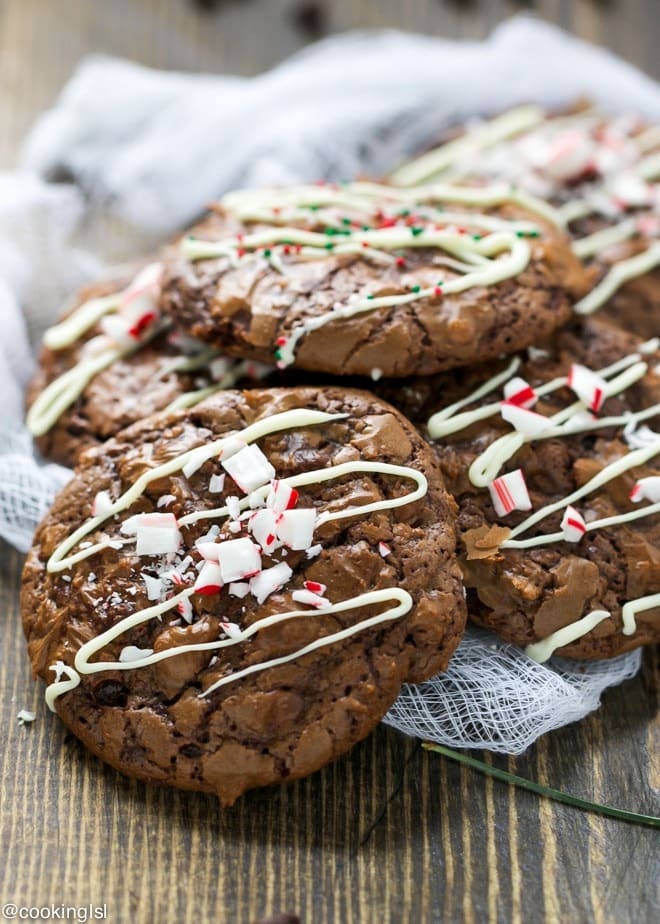 Bunch of brownie cookies on a wooden table drizzled with white chocolate sauce and sprinkled with chopped candy sugar. 