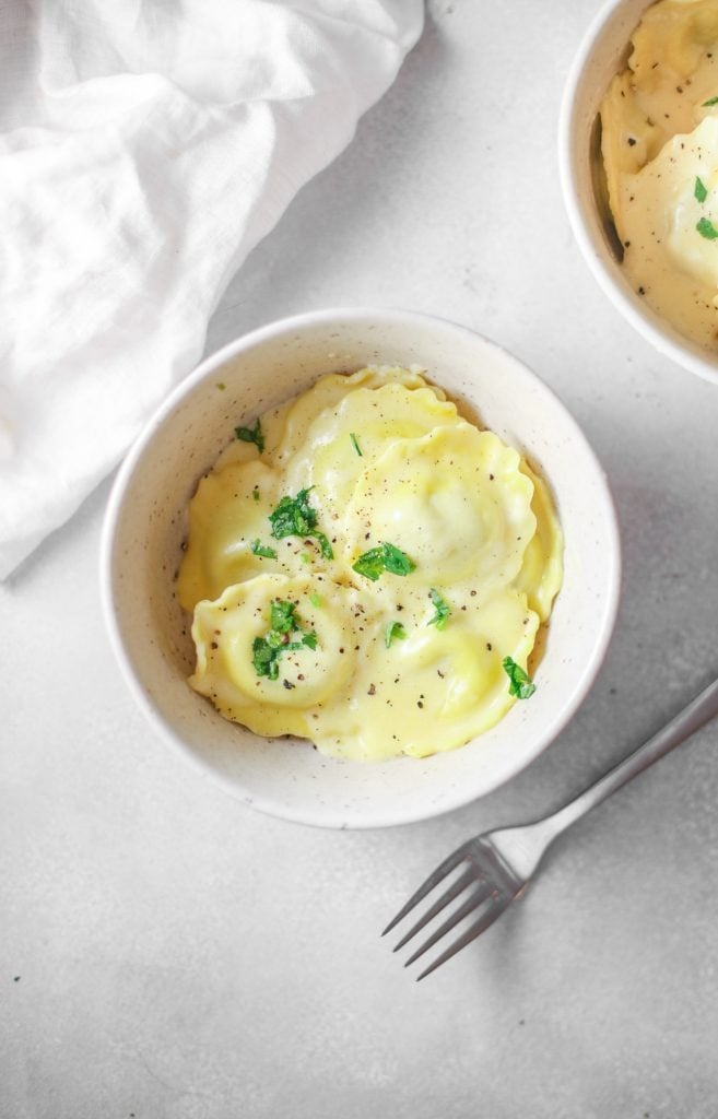 Cheesy ravioli on a white bowl garnished with chopped parsley leaves. 