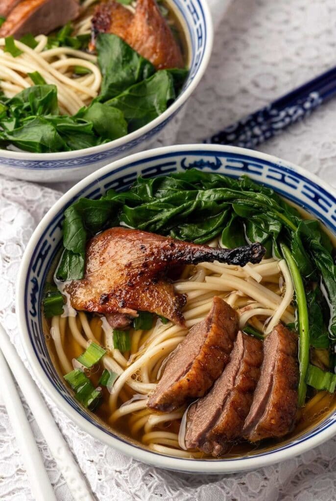 Noodle soup with broth, sliced roast duck, and greens served on a Chinese bowl. 