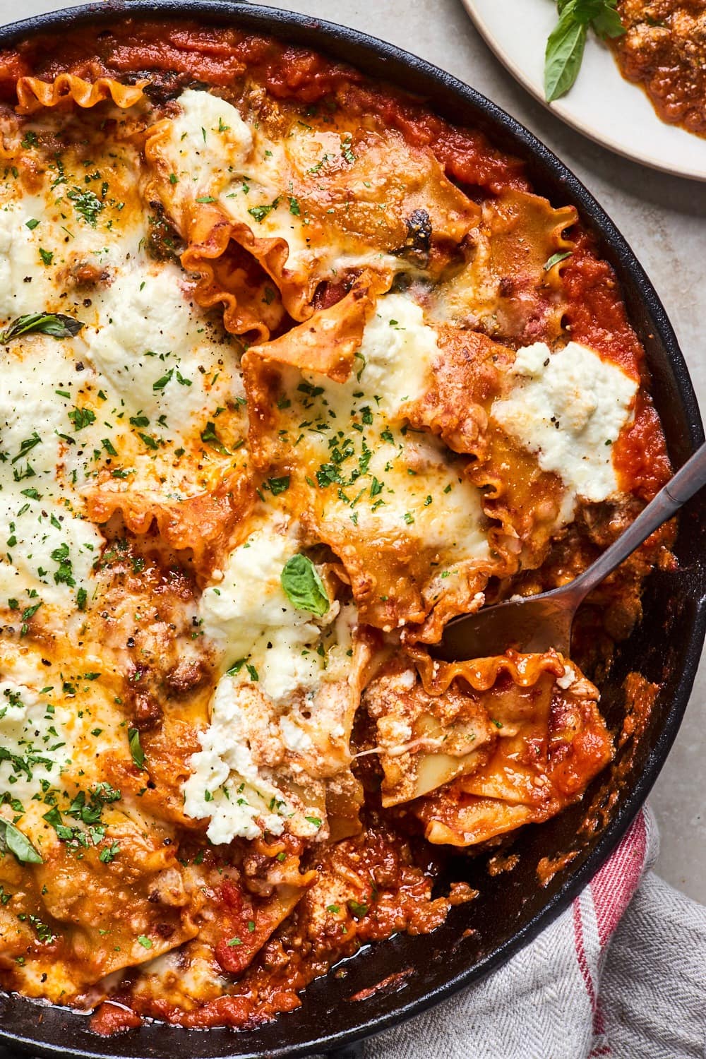 Layers of pasta lasagna with tomato sauce and melted cheese on a cast iron pan