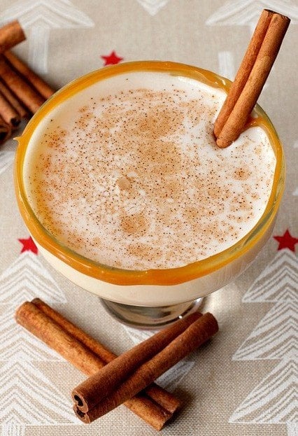 Eggnog cocktail served in a caramel rimmed glasses sprinkled with cinnamon powder on top.