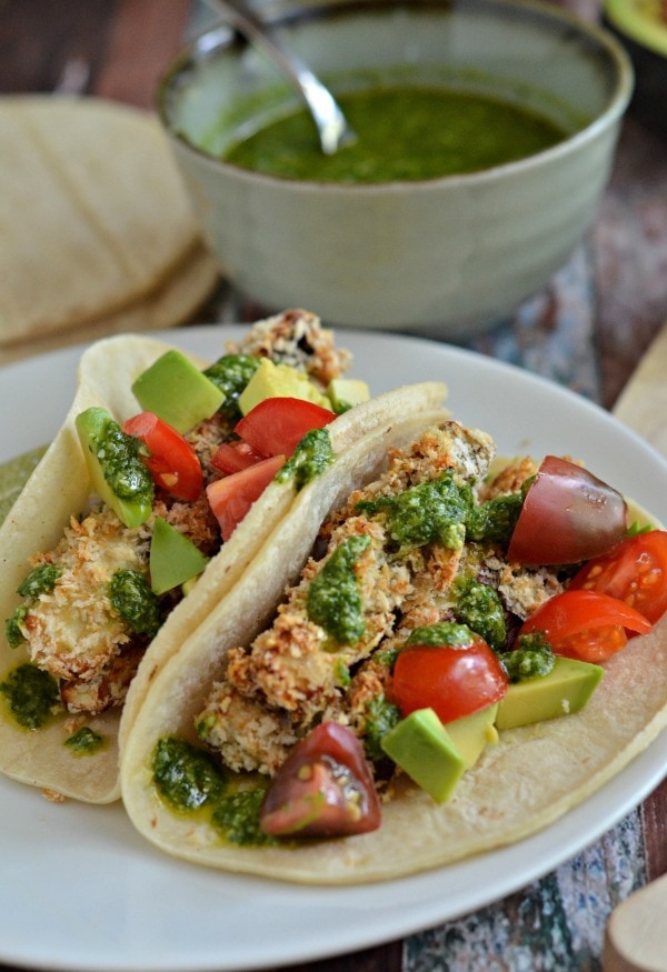 Taco shells with eggplant salad filling made with garlic, cilantro, mustard, lime juice, honey, olive oil, and Parmesan cheese served on a white plate. 