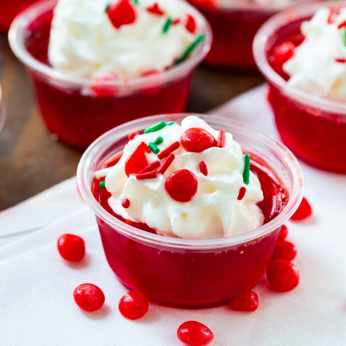 Fireball Jello shots on plastic cups topped with whipped cream and fresh cranberries garnish.