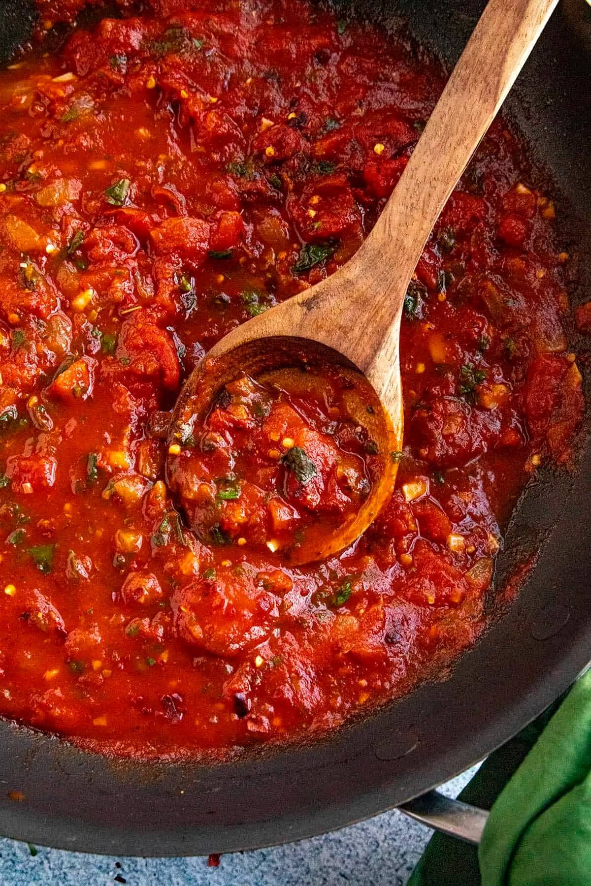 Wooden spoon mixing Fra diavolo sauce cooked on a skillet pot. 