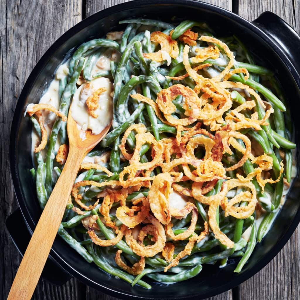Green bean casserole in a black dish with wooden spoon. 