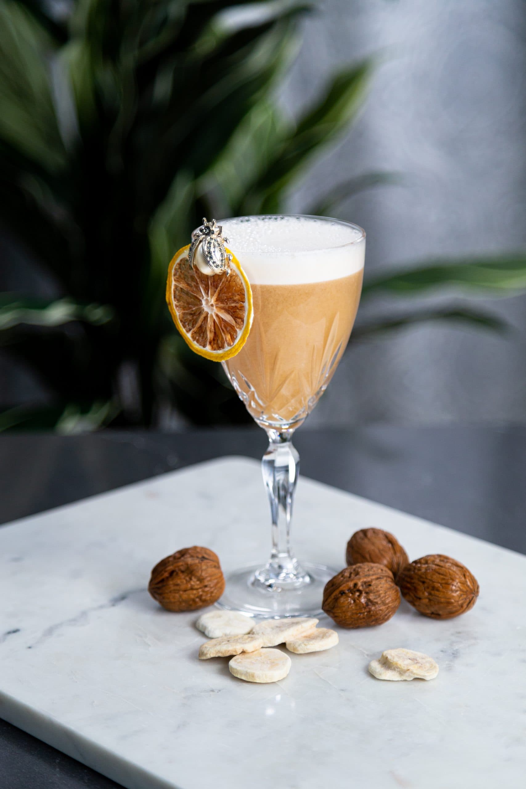 Banana Stand cocktail infused with banana, chocolate, walnut bitters, and lemon with egg white foam and dried lemon wheel garnish