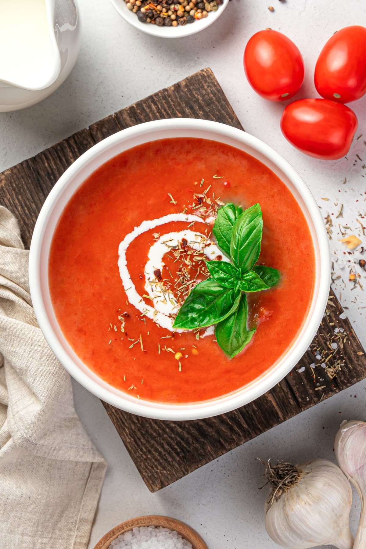 Bowl of Homemade Basil Tomato Soup with Cream on a Wooden Board