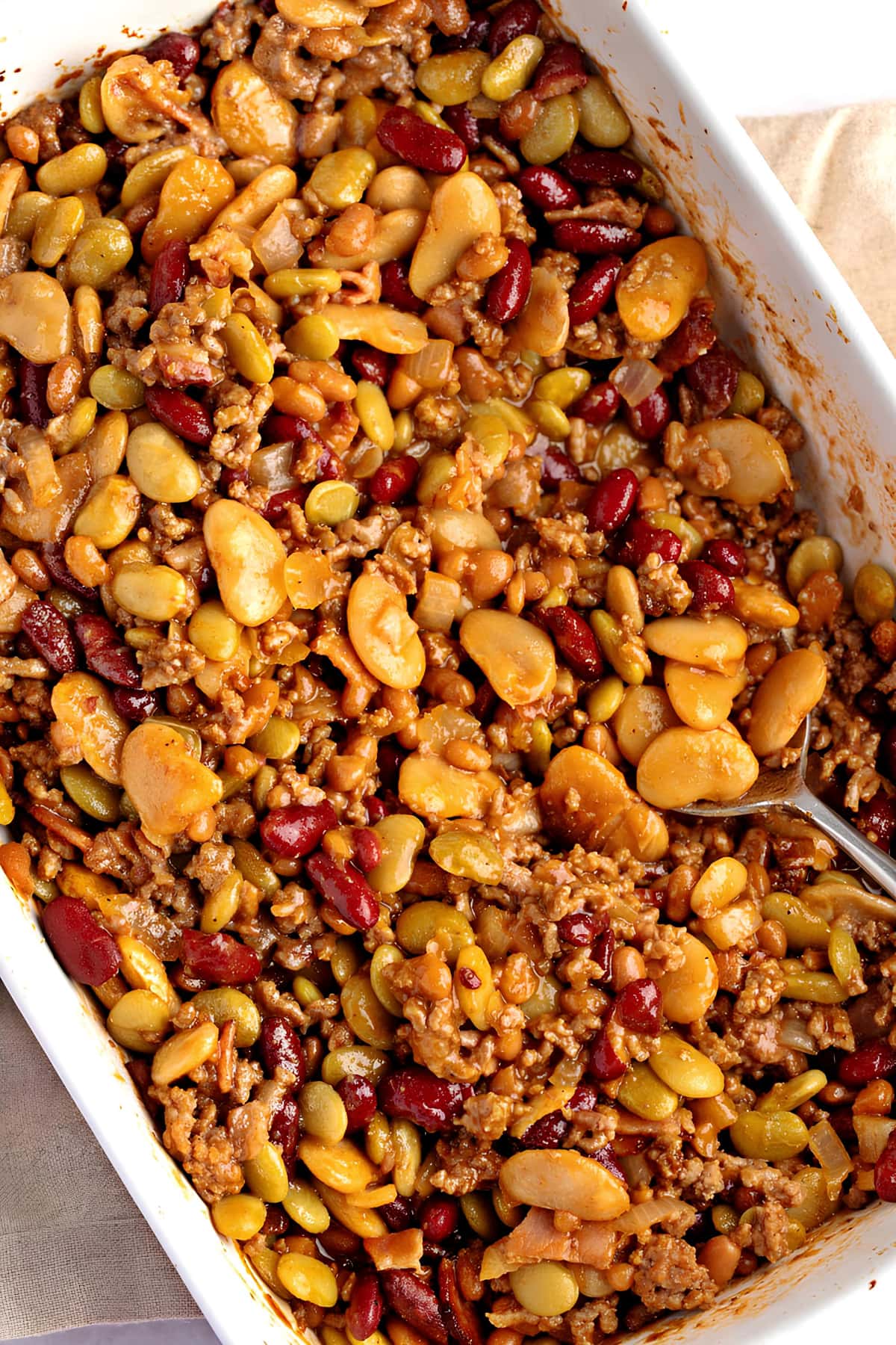 Homemade sweet and savory calico beans with ground beef in a white casserole