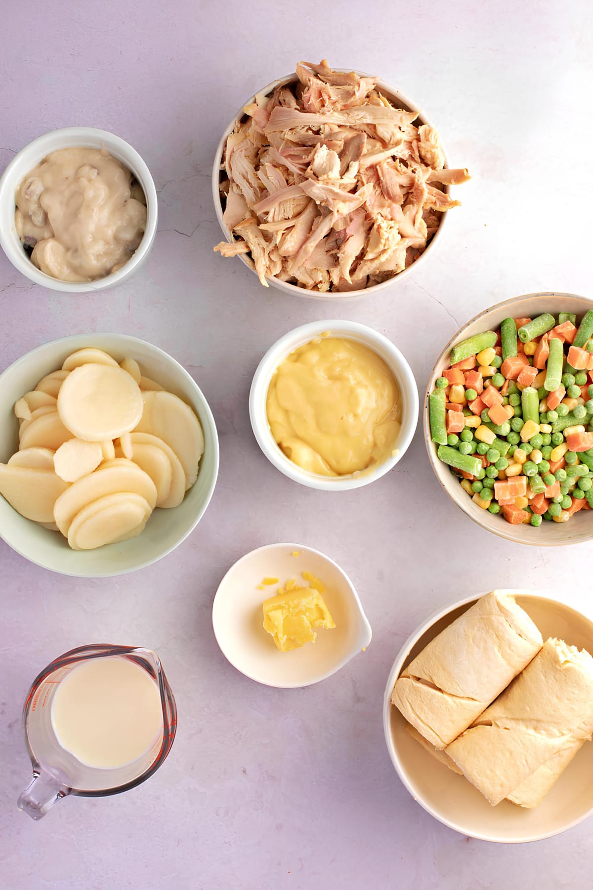 Bowls of Ingredients for Chicken Pot Pie with Crescent Rolls Including Butter, Vegetables, Cream of Chicken and Mushroom Soup, Milk, Salt and pepper