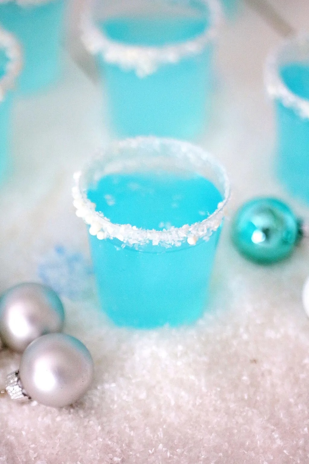 Blue Jello shots on sprinkle candies-rimmed plastic cups on holiday table. 
