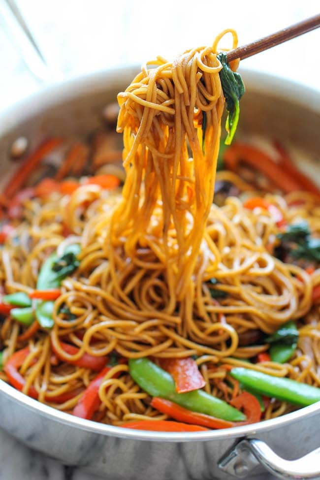 Chopsticks picking Chinese noodles with vegetables on a pan.