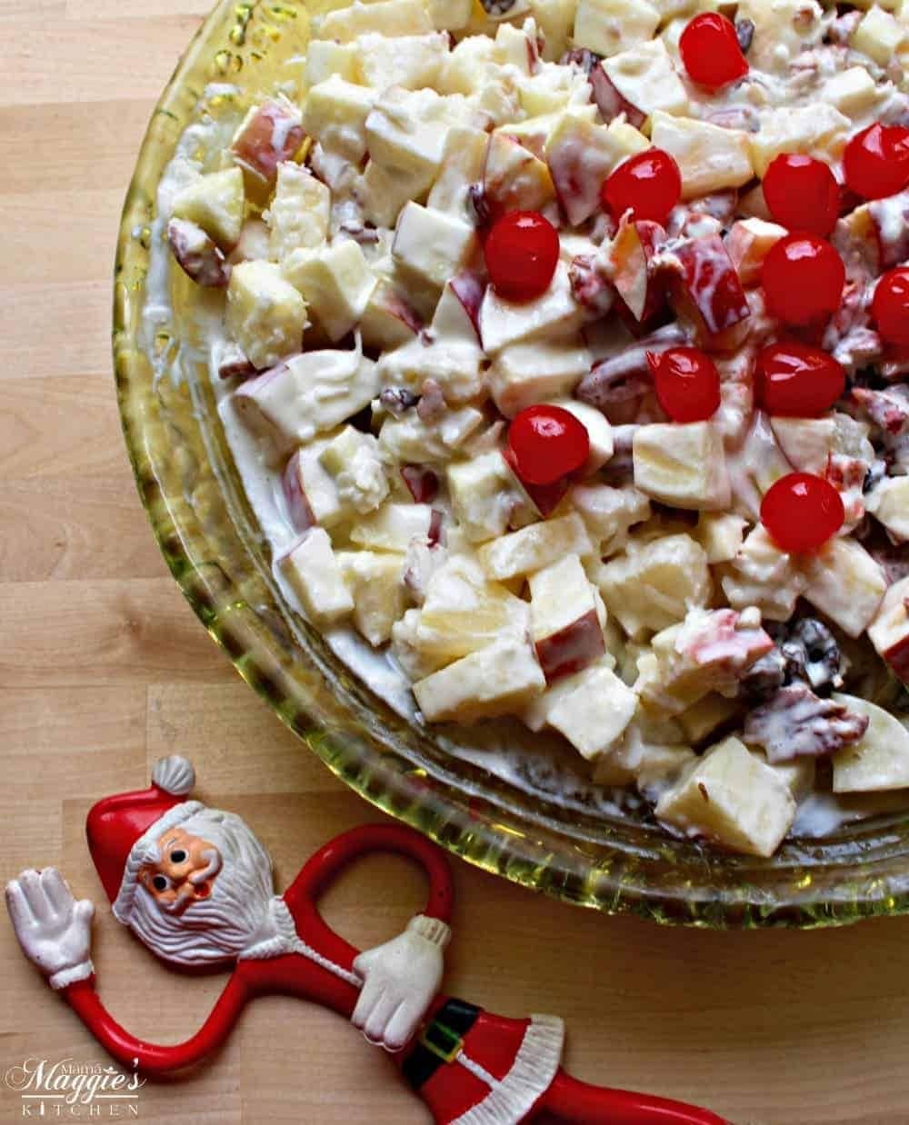 Salad made with fresh apples, canned pineapple, maraschino cherries, pecans, coconut, and raisins on a glass bowl. 