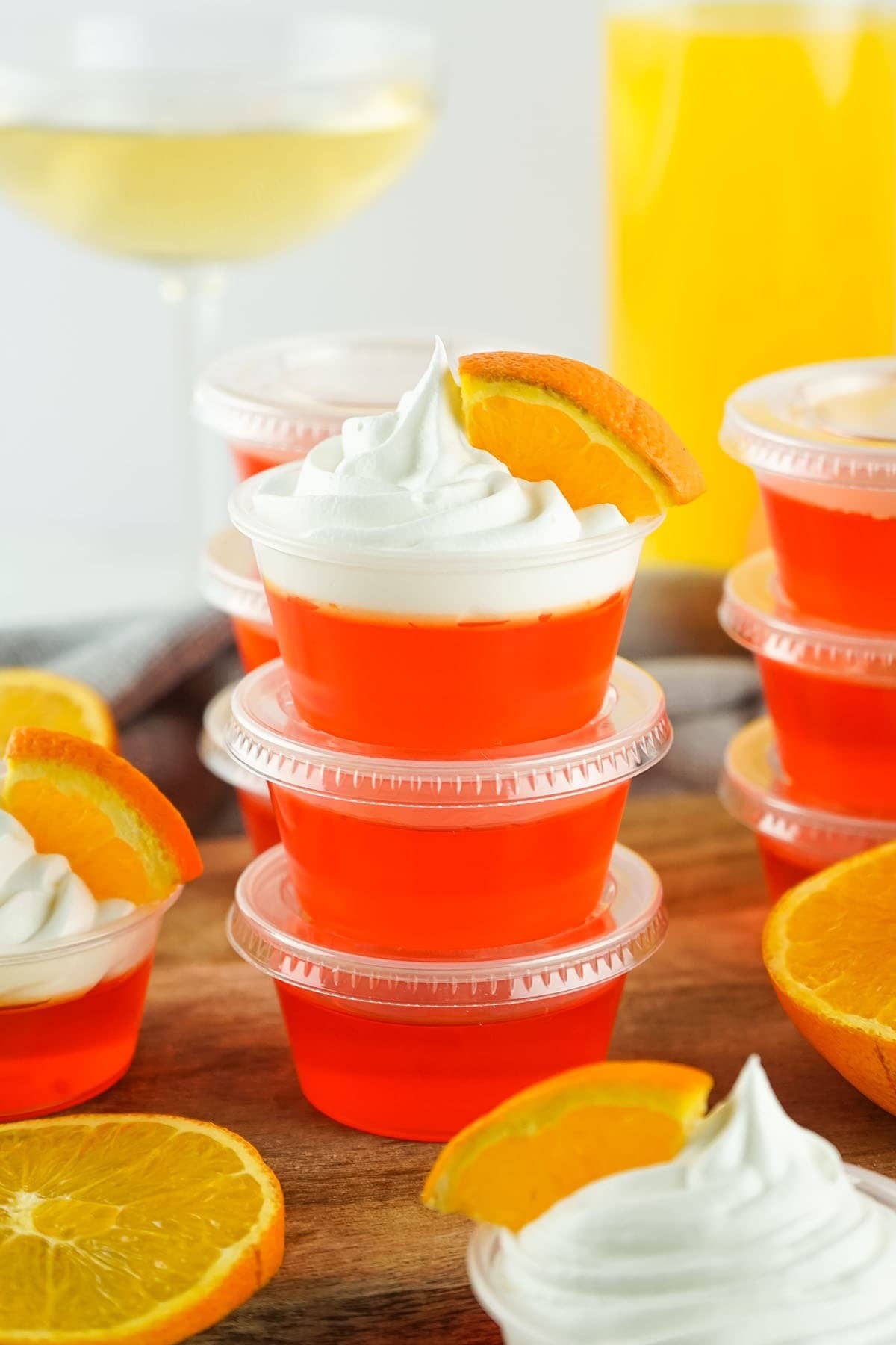 Stack of Mimosa Jello shots on plastic cups garnished with shipped cream and orange slices.