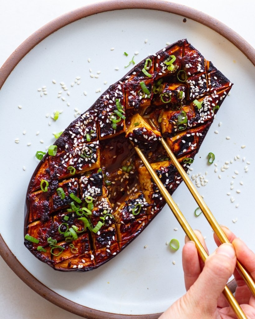 Hand picking a piece of  a baked glazed eggplant using a golden chopsticks. 