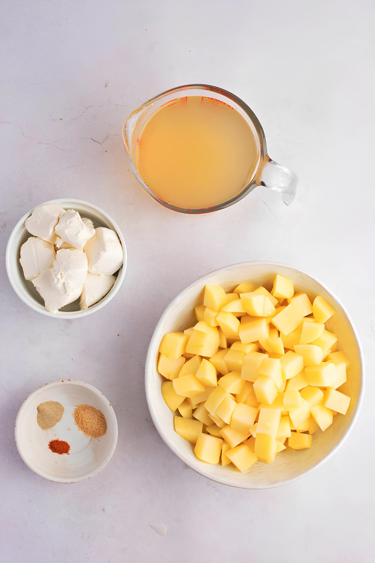 Diced potatoes, cheese, broth and seasoning on top of white surface. 