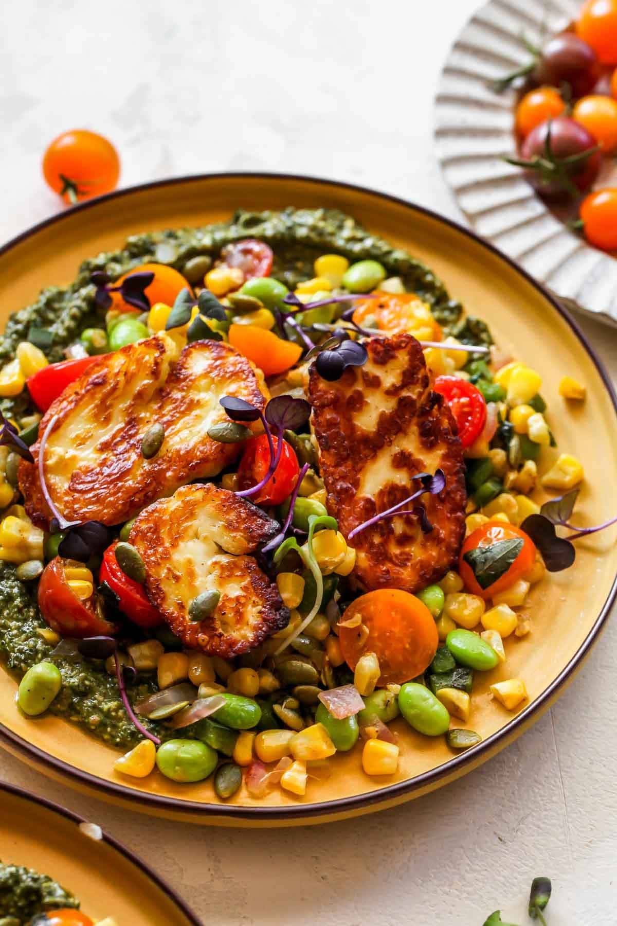 Pesto corn succotash with fried halloumi served on a plate.