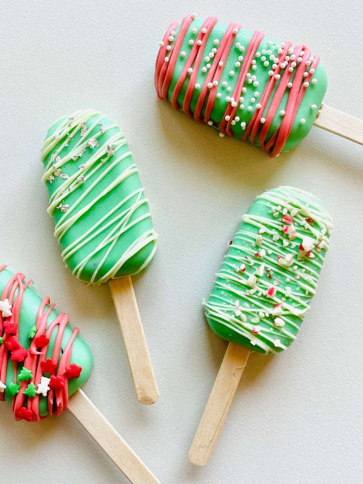 Pieces of popsicle cake pops covered with green-colored melted chocolate decorated with red and white drizzles and sprinkles 