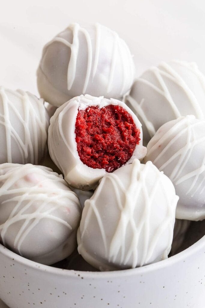 A bunch of white chocolate-covered cake pops with a sliced red velvet cake pop placed on top, all arranged in a bowl.