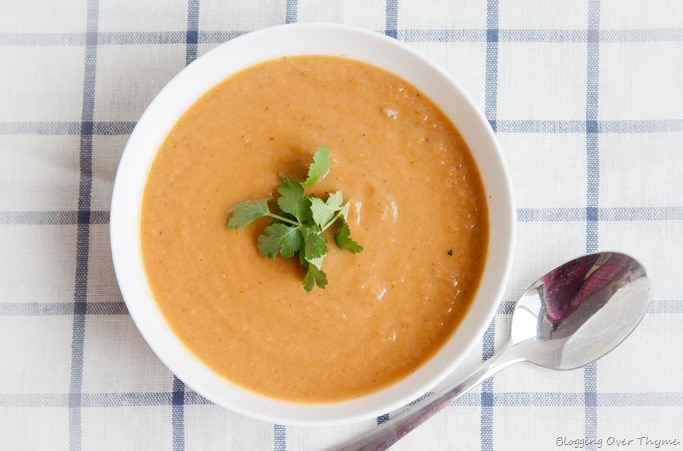 Top view of a bowl of roasted eggplant soup topped with parsley leaves and spoon on the side. 